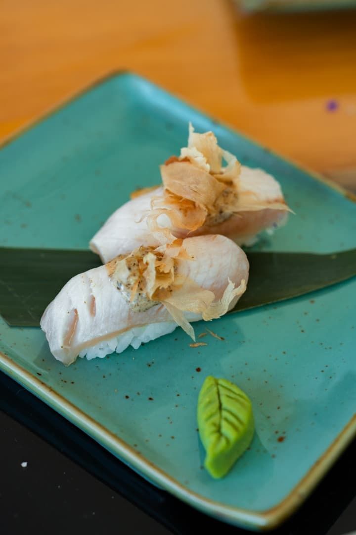 Dos piezas de sushi blanco con jengibre sobre un plato color turquesa, adornadas con una hoja verde.