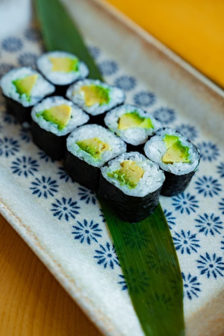 Rollos de sushi en un plato estampado con guarnición verde y envoltorios de alga oscura.