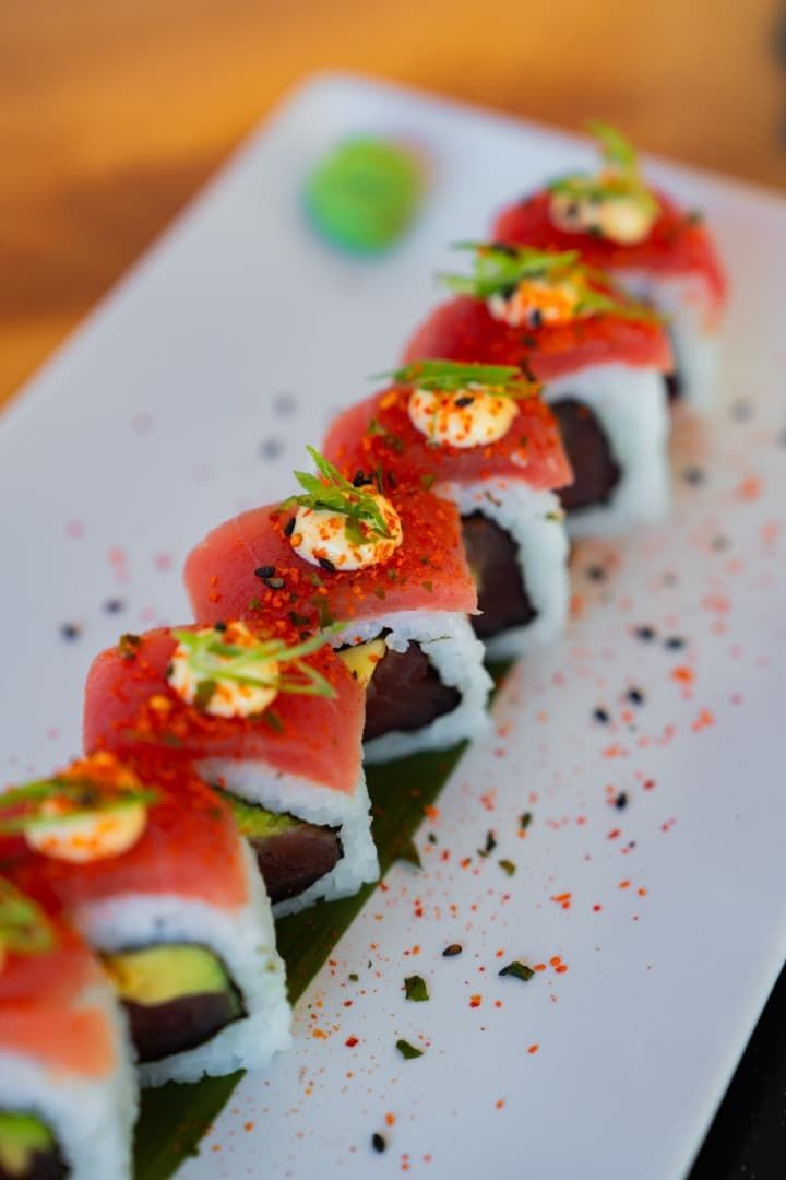 Rollos de sushi cubiertos con fresas en rodajas y salsa en un plato blanco, adornados con hierbas.