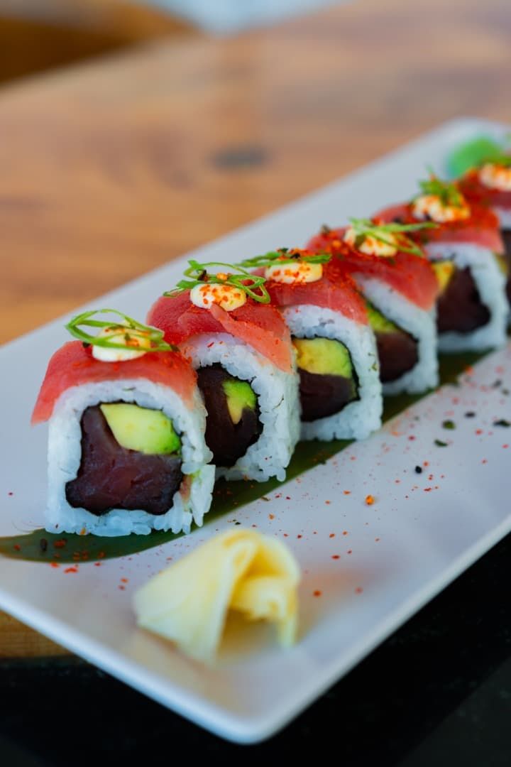Rollos de sushi cubiertos con pescado rojo y guarnición verde en un plato blanco.