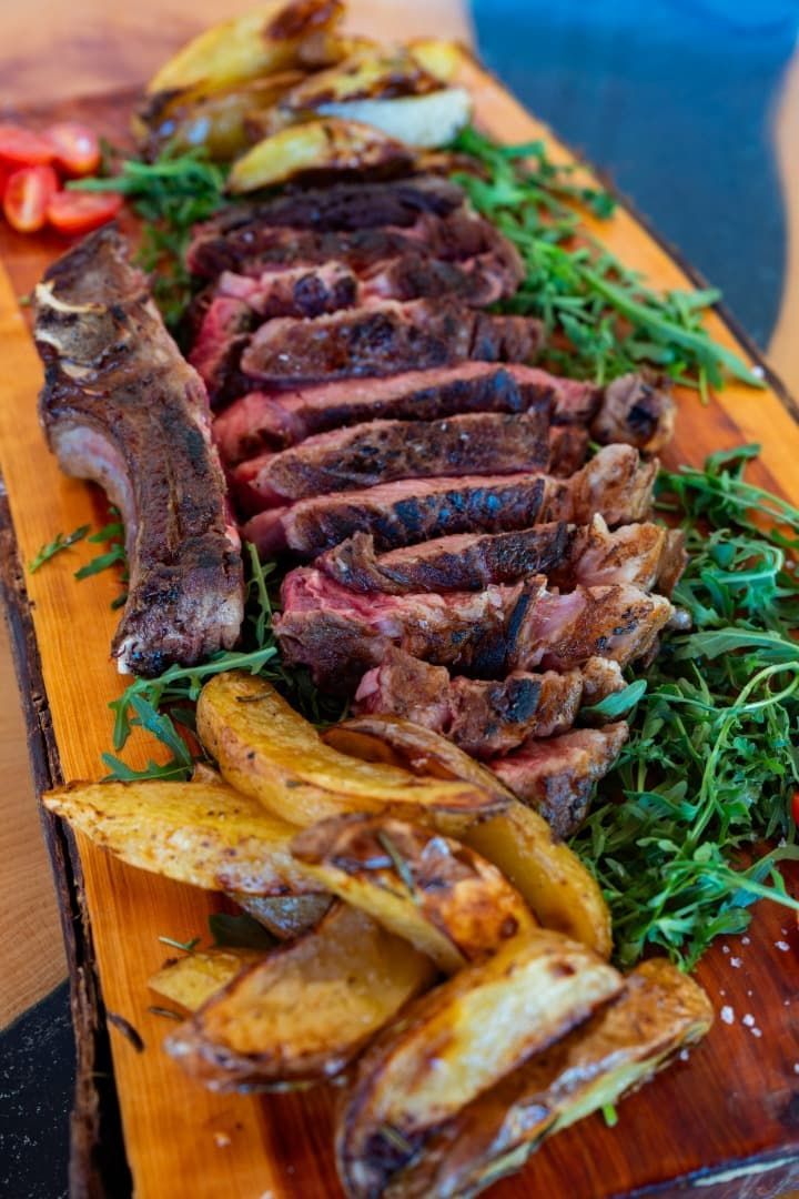 Filete a la parrilla en rodajas con verduras asadas y hojas verdes en una fuente de madera.