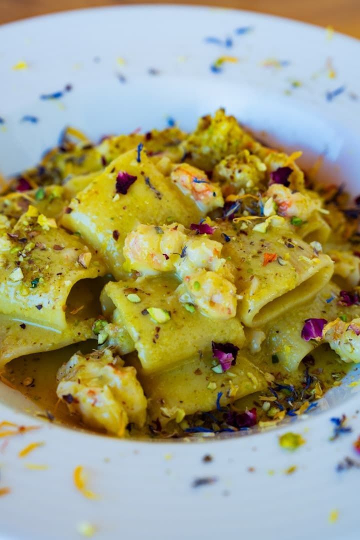 Pasta en salsa cremosa amarilla con hierbas y hojuelas de pimiento rojo en un plato blanco.