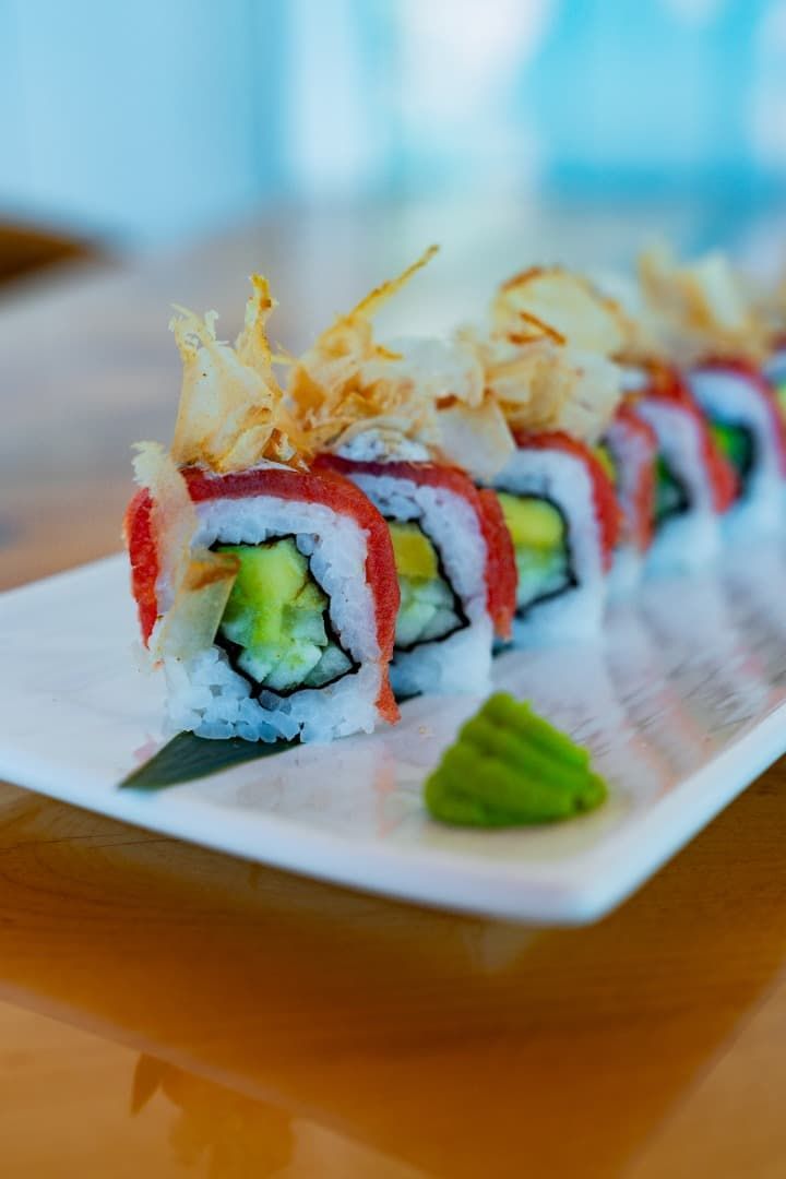 Rollitos de sushi cubiertos con una guarnición crujiente, servidos en un plato blanco con wasabi aparte.