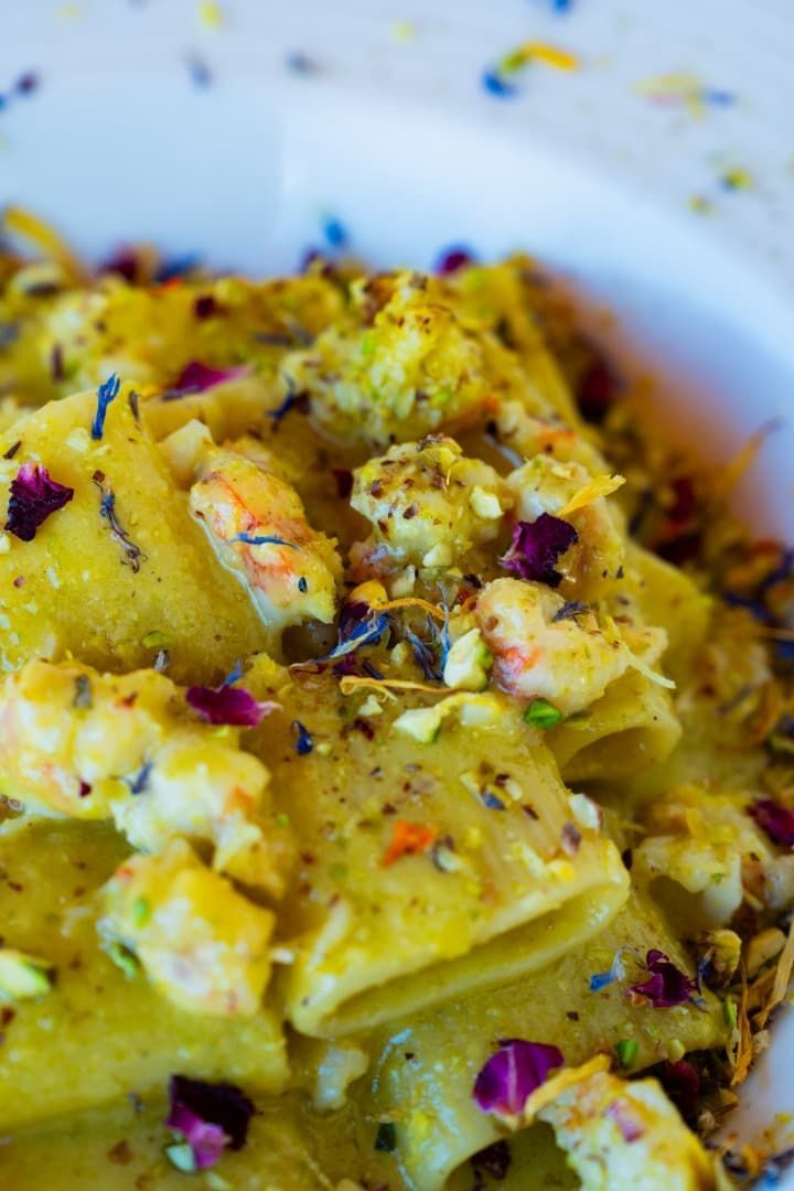 Arroz amarillo con azafrán, verduras y pétalos de flores moradas en un plato blanco.