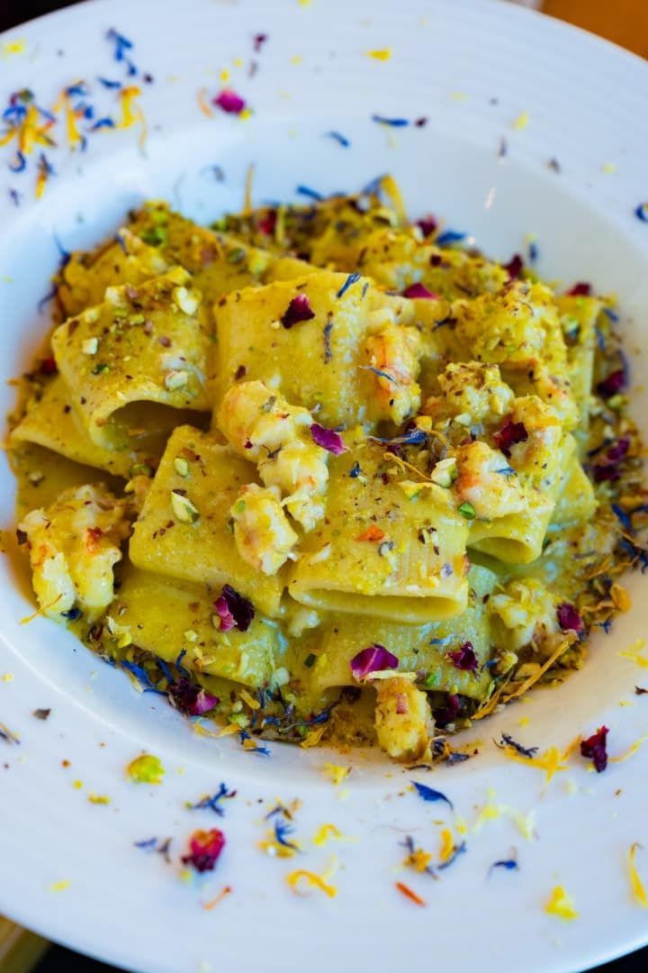 Pasta cremosa en un plato blanco, cubierta con hierbas y una colorida guarnición.