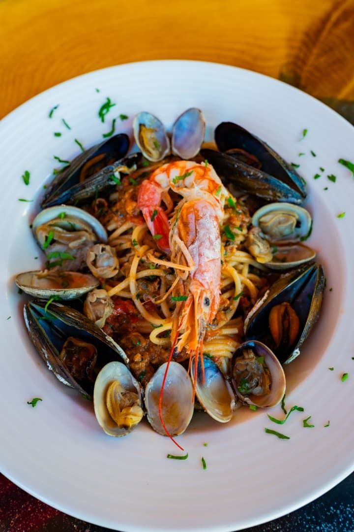 Pasta con mariscos, con gambas y mejillones, servida en un bol blanco y adornada con hierbas aromáticas sobre una mesa de madera.