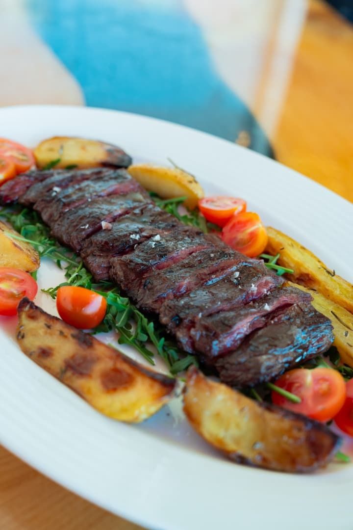 Medallones de carne a la parrilla con tomates cherry y patatas asadas en un plato blanco.