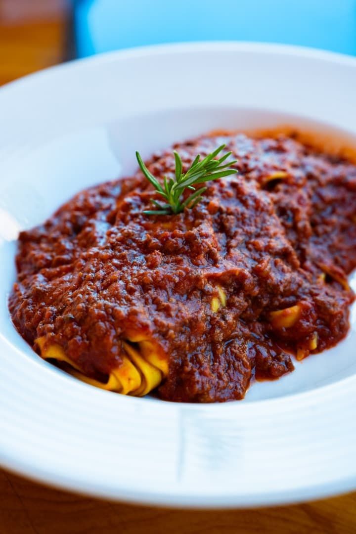 Plato de pasta con salsa de carne y guarnición de romero.