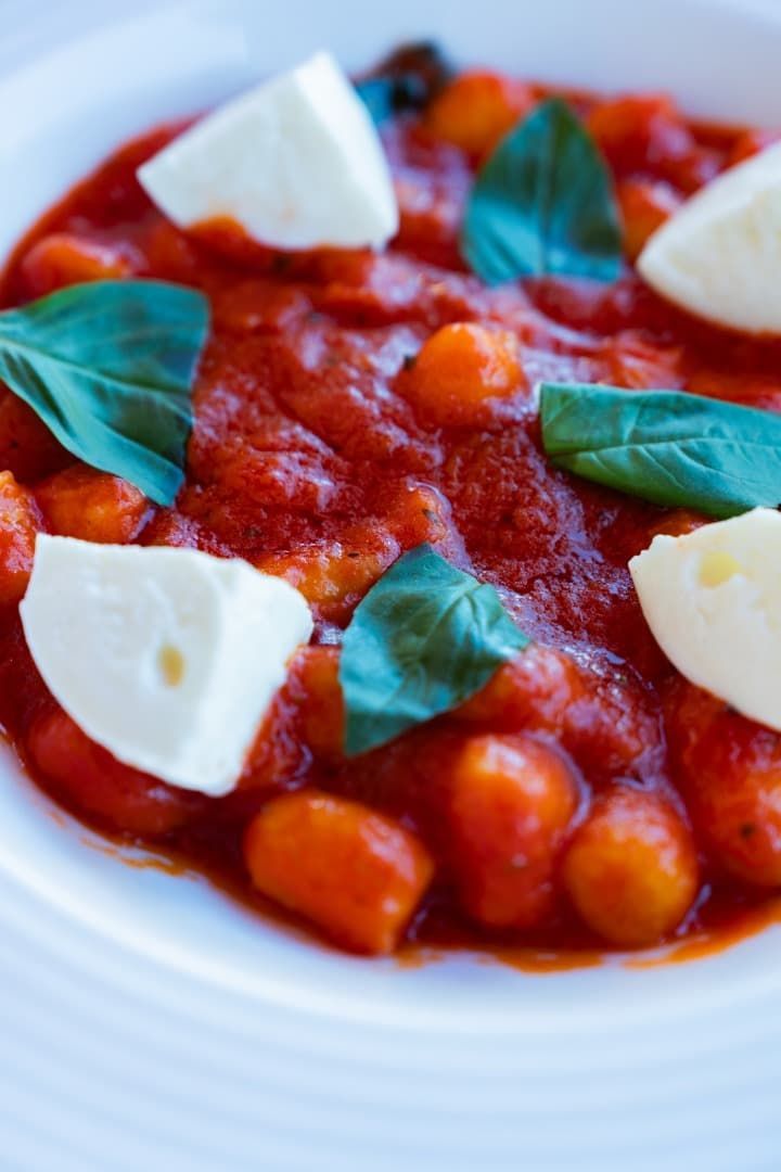 Pasta estilo Margarita con salsa de tomate, hojas de albahaca y mozzarella en un plato blanco.