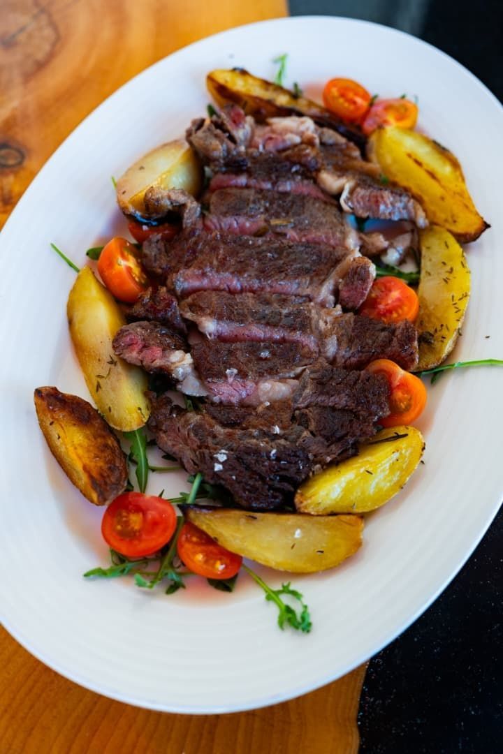 Filete en rodajas servido con patatas asadas y tomates cherry en un plato blanco.