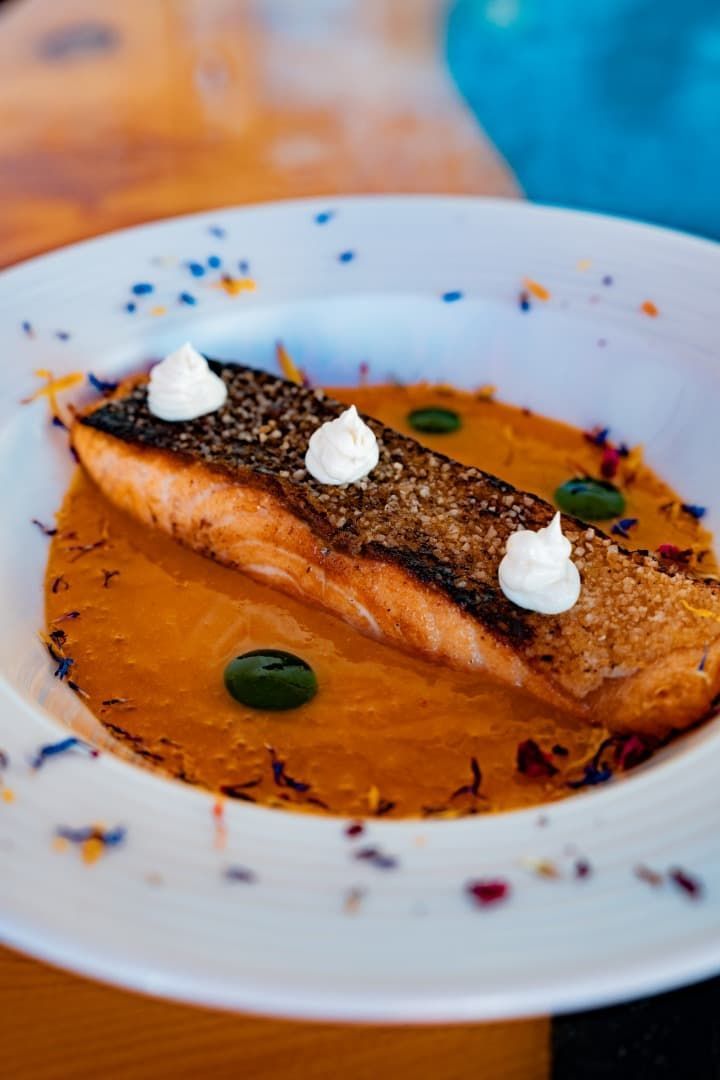 Salmón sellado en salsa de naranja sobre un plato blanco, adornado con hierbas verdes y unas cucharadas de crema.