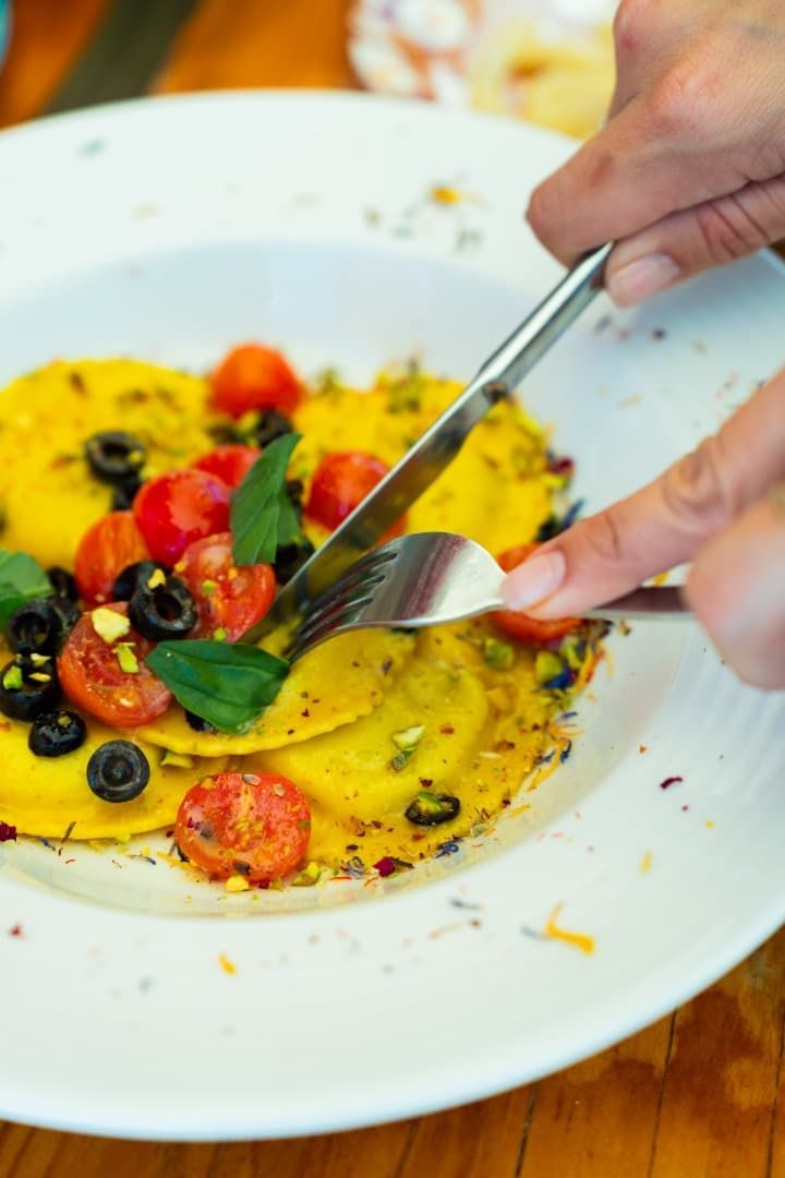 Manos emplatando un colorido plato de verduras en un plato blanco con un tenedor y una cuchara.