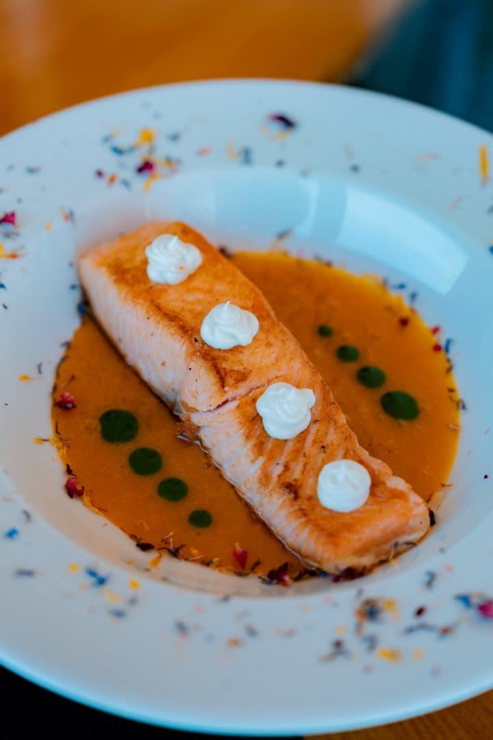 Filete de salmón emplatado con salsa de naranja y cucharadas de crema sobre un plato blanco.