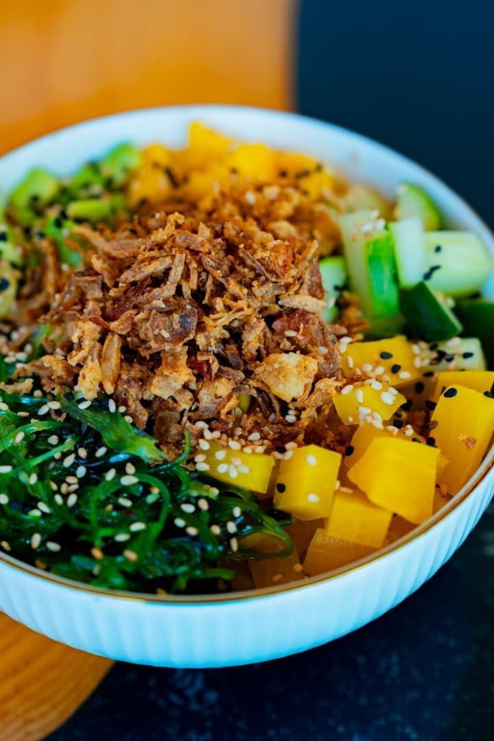 Poke bowl colorido con arroz, atún, aguacate, pepino, mango, verduras y semillas de sésamo.