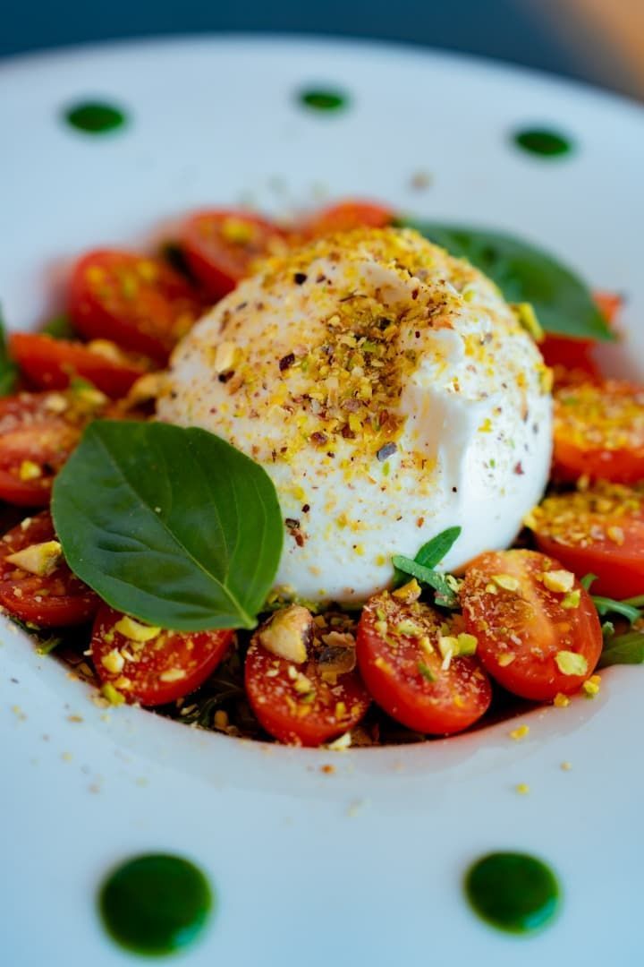 Ensalada Caprese con burrata, tomates cherry partidos por la mitad, albahaca y aceite de oliva en un plato blanco.