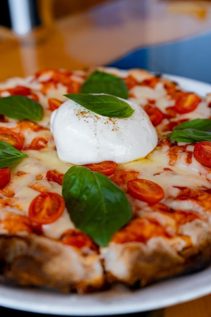 Pizza Margherita cubierta con albahaca fresca y una bola de burrata en un plato blanco.