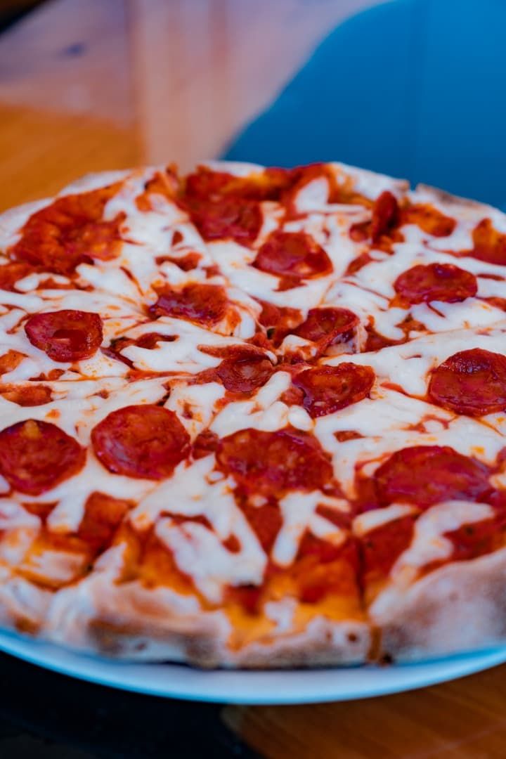 Pizza de pepperoni en un plato azul, con queso derretido y un fondo interior borroso.