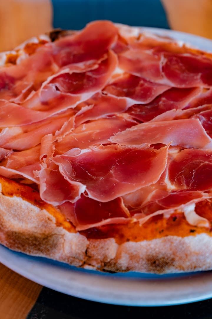 Pizza cubierta con finas lonchas de jamón serrano sobre un plato blanco.