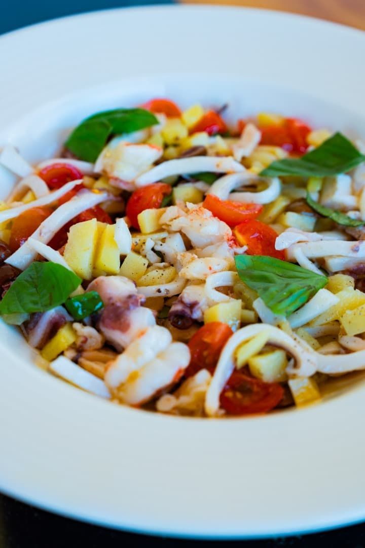 Plato de pasta colorida con albahaca fresca y verduras picadas en un plato blanco.