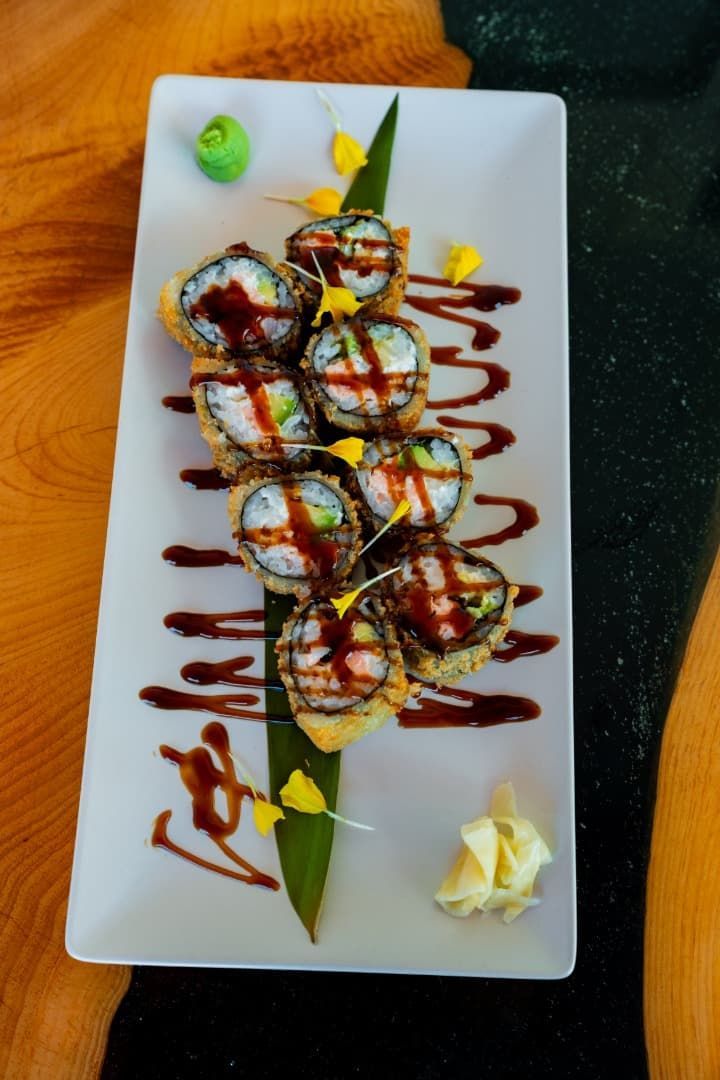 Rollos de sushi bañados en salsa sobre un plato rectangular blanco, adornados con wasabi y jengibre encurtido.