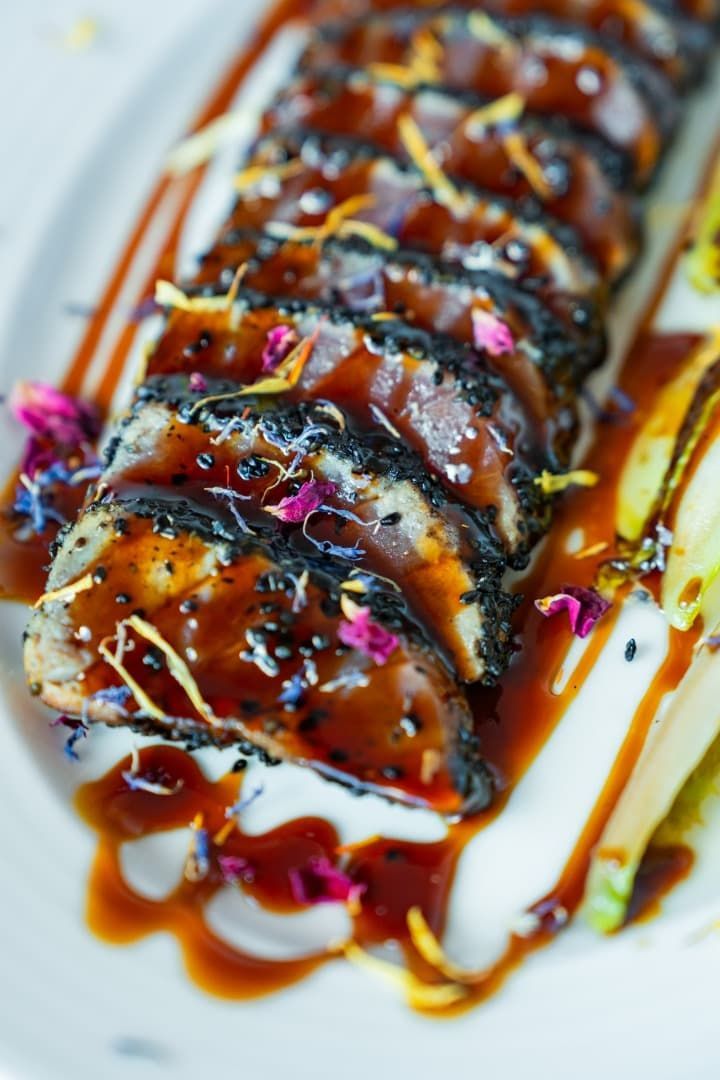 En una cocina, un chef emplata rollos de sushi en una bandeja blanca junto a cuencos con guarniciones.