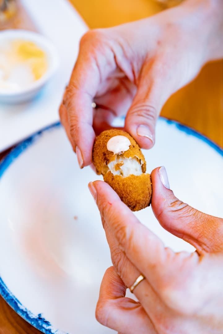 Manos partiendo un bocadillo frito con relleno cremoso sobre un plato blanco.
