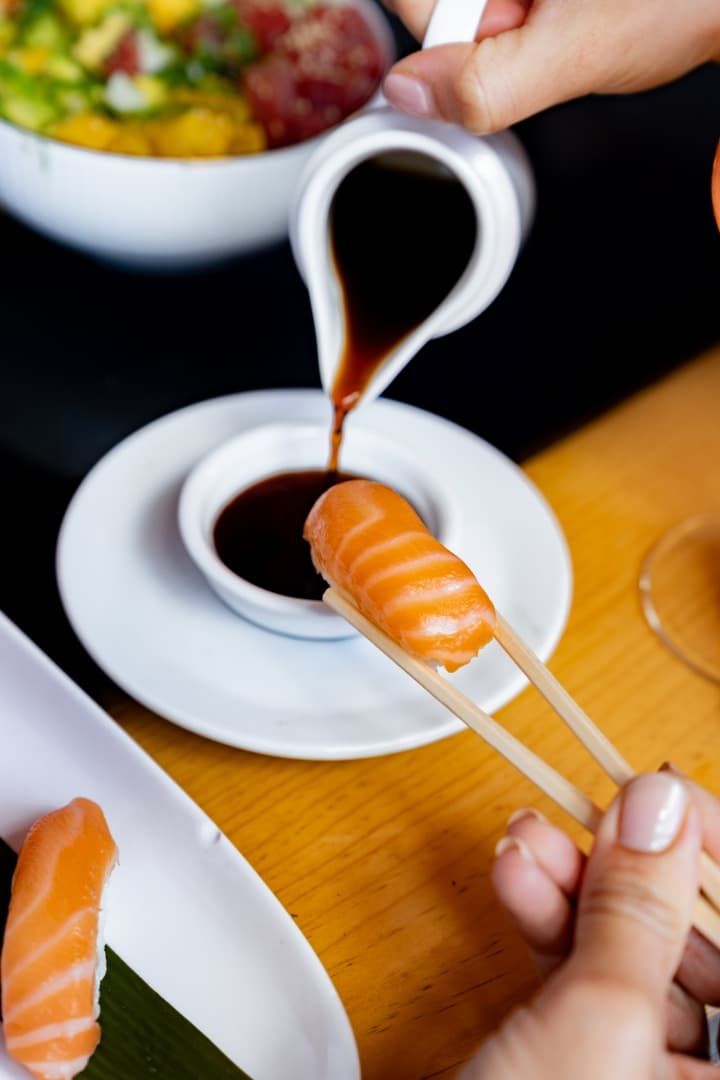 En la mesa de un restaurante, se está sirviendo sushi en salsa de soja, mientras una mano sostiene los palillos.