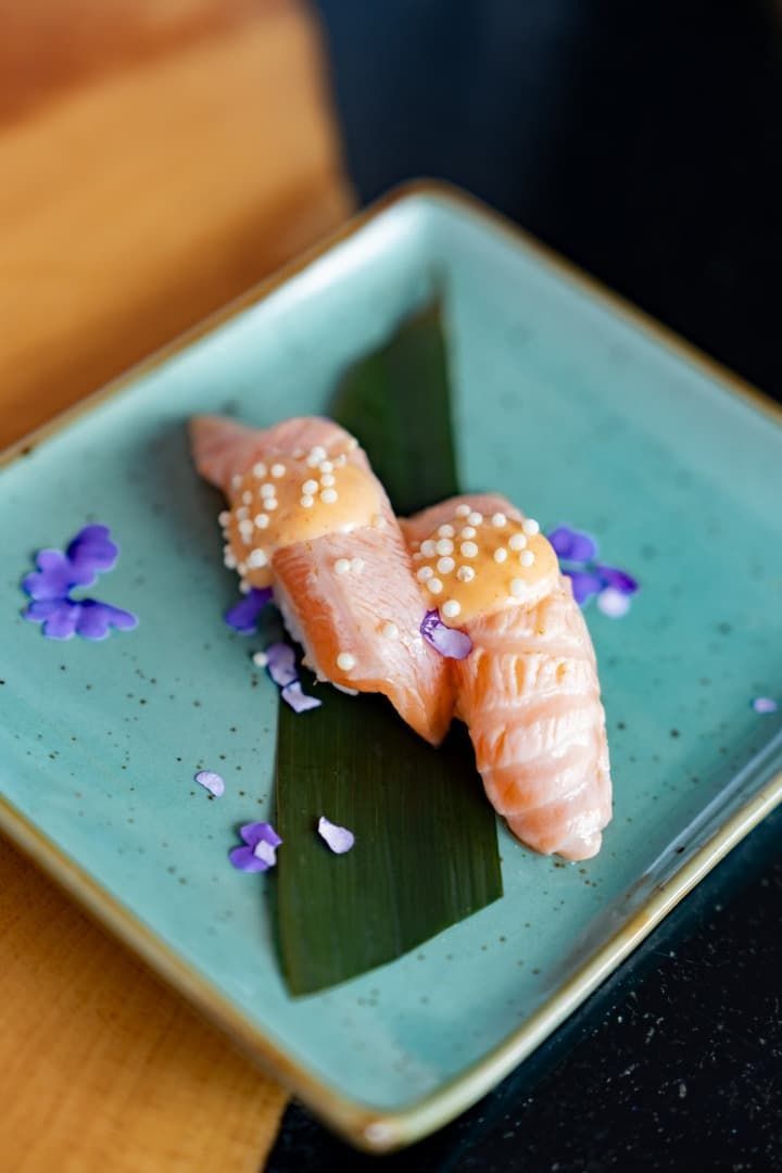 Dos piezas de sushi en un plato turquesa con guarnición morada sobre una mesa de madera.
