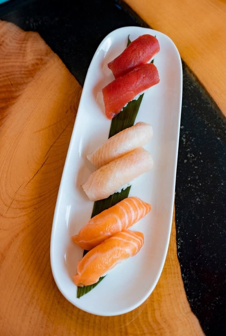 Surtido de nigiri de sushi en un plato blanco alargado sobre una mesa de madera.