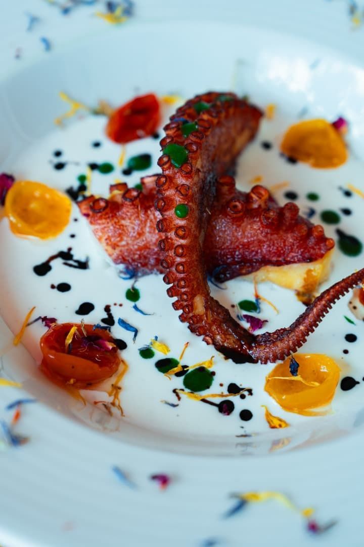 Pulpo a la parrilla en un plato blanco con salsas coloridas y guarnición de hierbas.