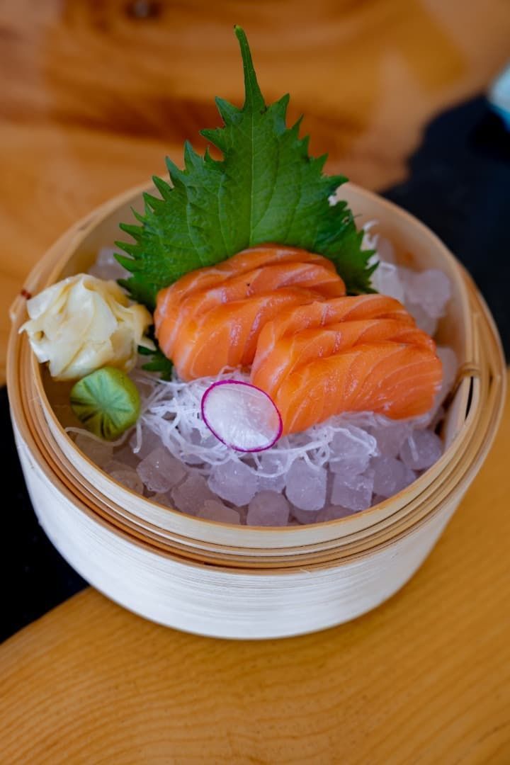 Plato de sushi con nigiri de salmón, daikon rallado, rodajas de rábano y wasabi en un tazón pequeño.
