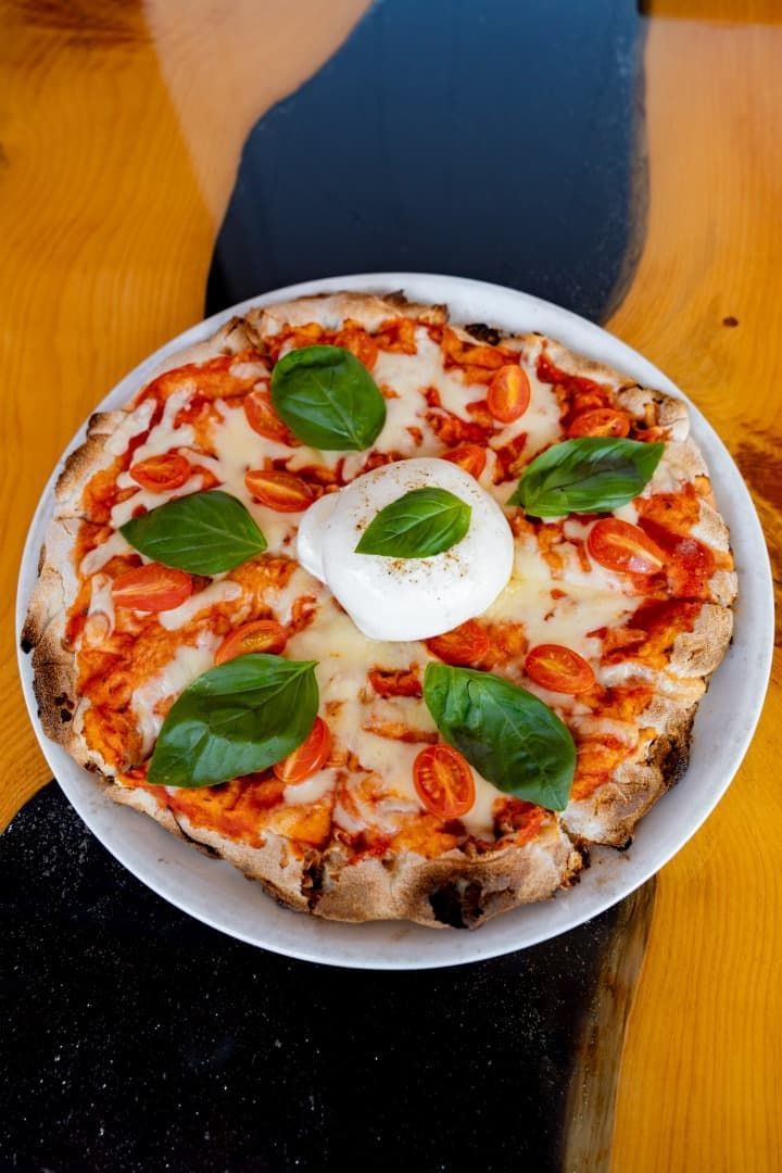 Pizza Margarita con hojas de albahaca y queso fundido en un plato blanco sobre una mesa de madera.