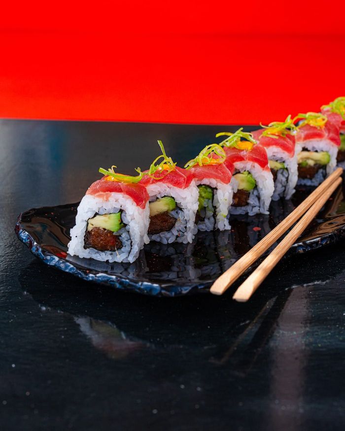 Una persona está comiendo sushi con palillos en un plato.