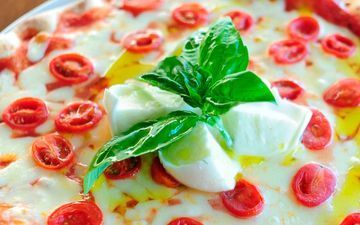 Una pizza con tomates, mozzarella y albahaca en un plato.