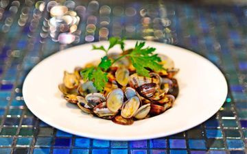 Un plato blanco cubierto con almejas y perejil sobre una mesa.