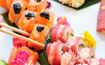 Una persona está comiendo sushi con palillos en un plato.