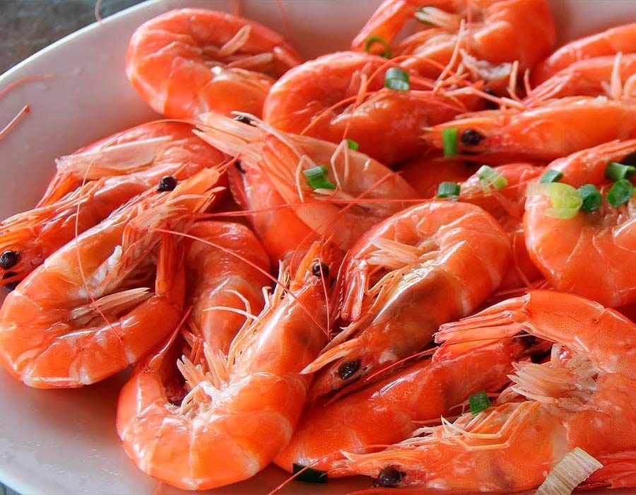 Un plato blanco cubierto con camarones y cebollas verdes.
