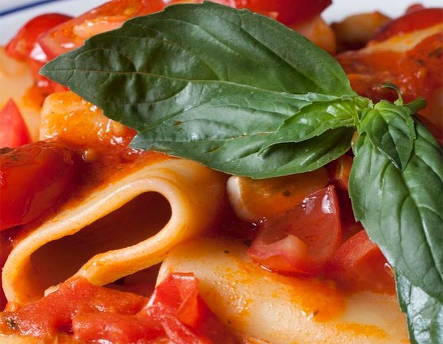 Un primer plano de un plato de pasta con salsa de tomate y hojas de albahaca.