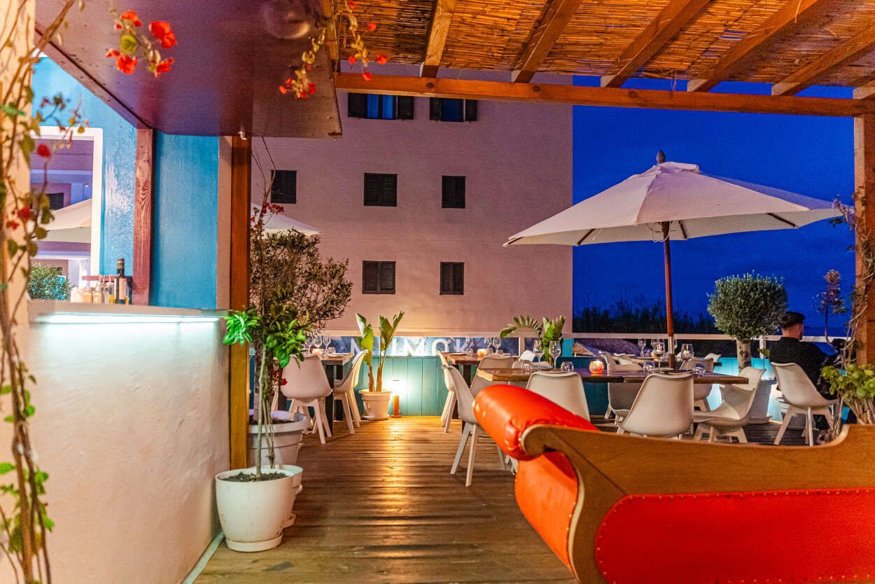 Un restaurante con mesas, sillas, sombrillas y un sofá rojo.