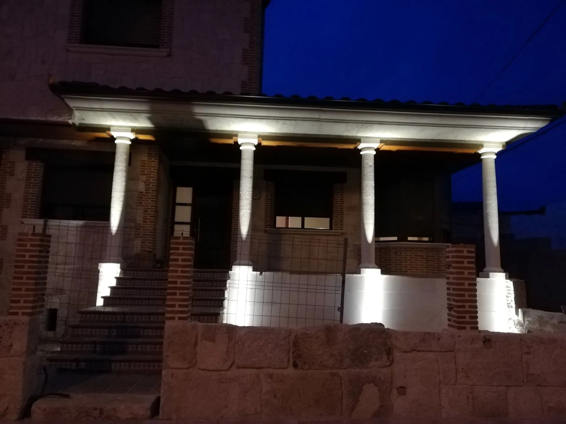 Un porche con columnas y escaleras se ilumina por la noche.