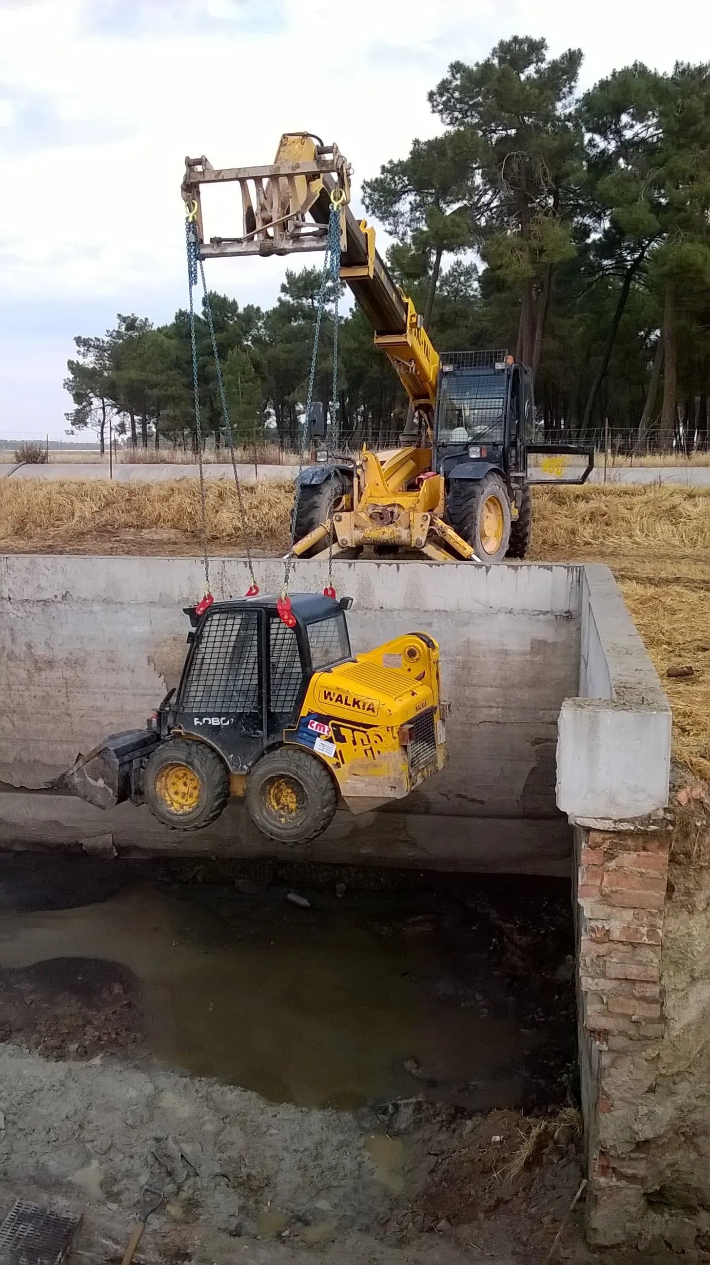 Un tractor amarillo es levantado por una grúa sobre un puente.