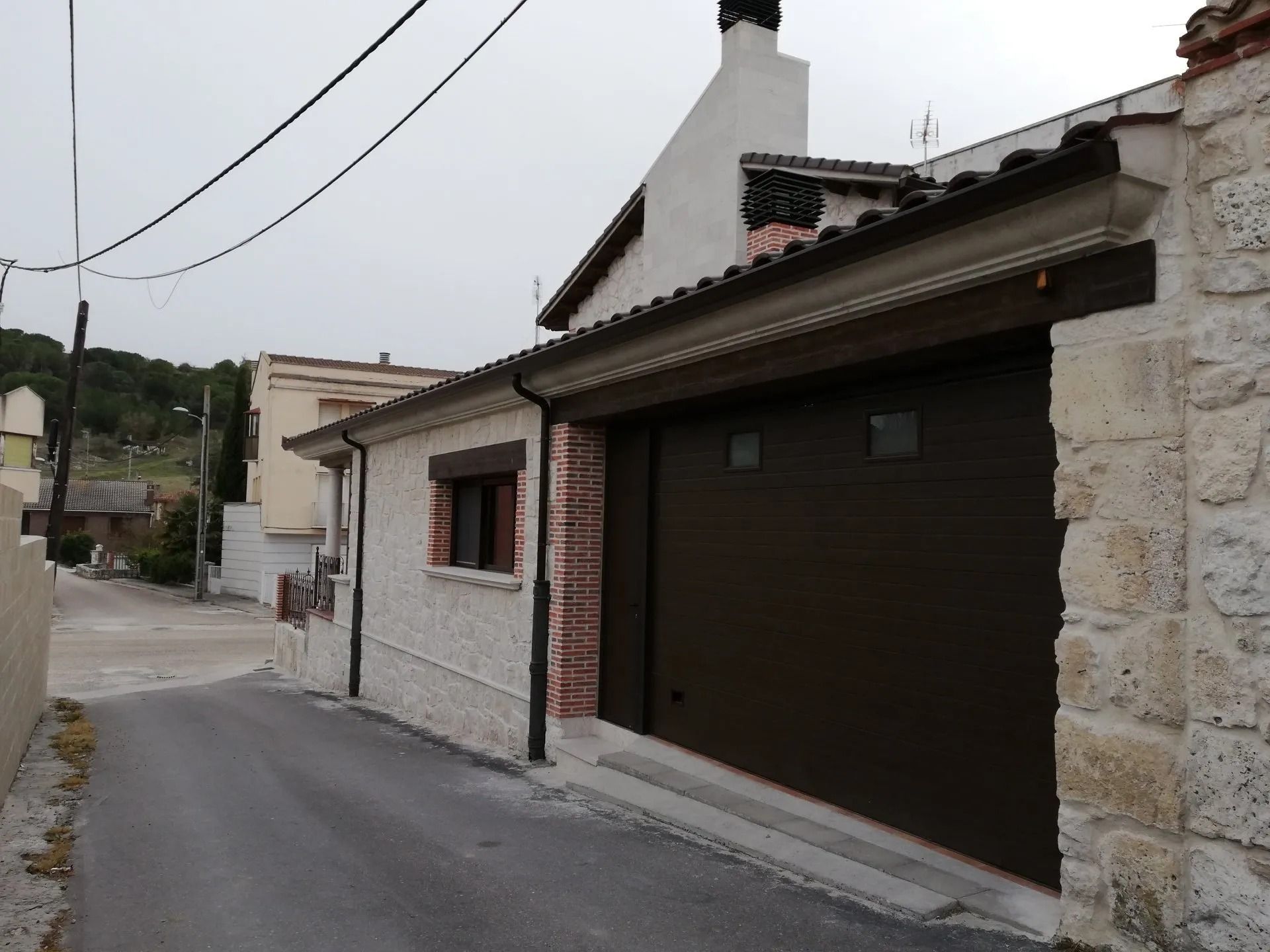 Una casa con una puerta de garaje marrón y un muro de piedra.