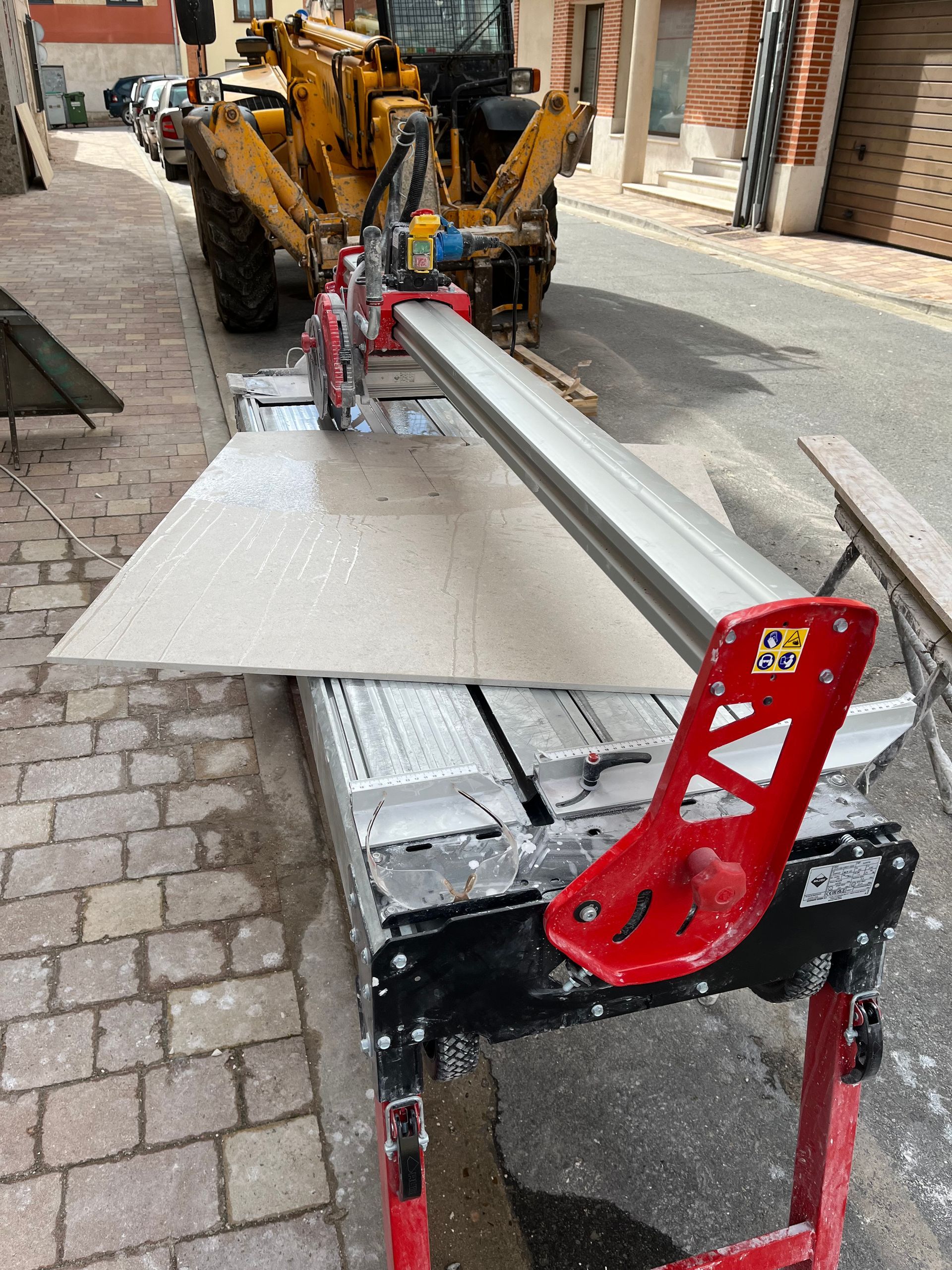 Un cortador de azulejos está sentado en una acera de ladrillos junto a un tractor amarillo.