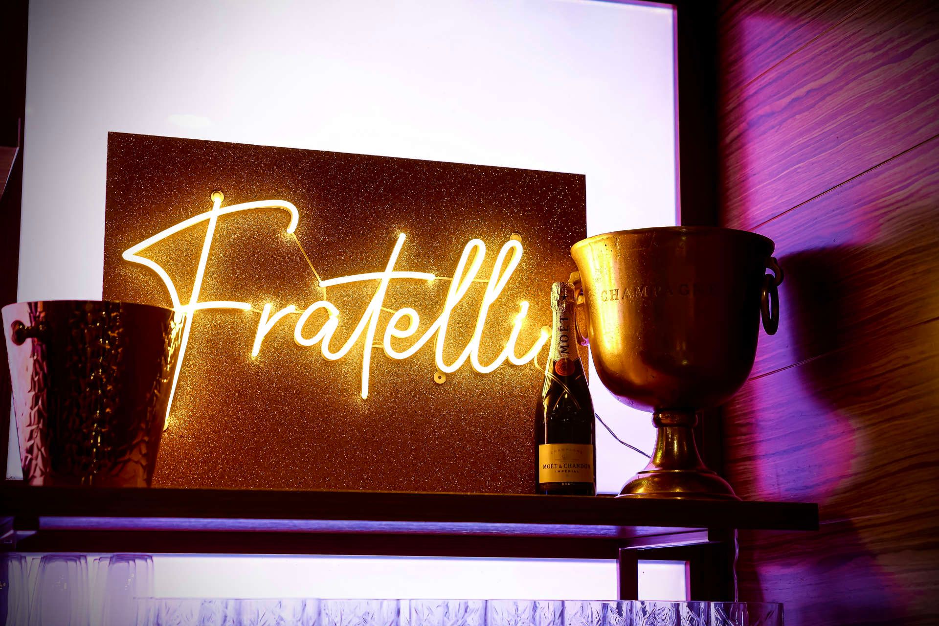 eine Flasche champagner steht neben einem neonschild mit dem wort fratelli