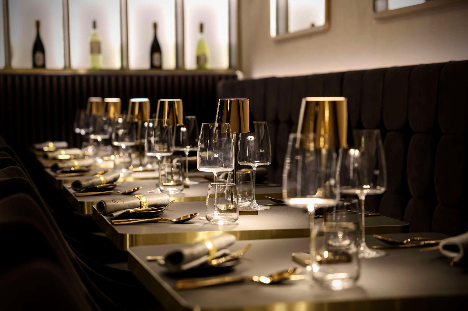 eine Reihe von Tischen mit Gläsern , Tellern , Löffeln und Lampen in einem Restaurant .