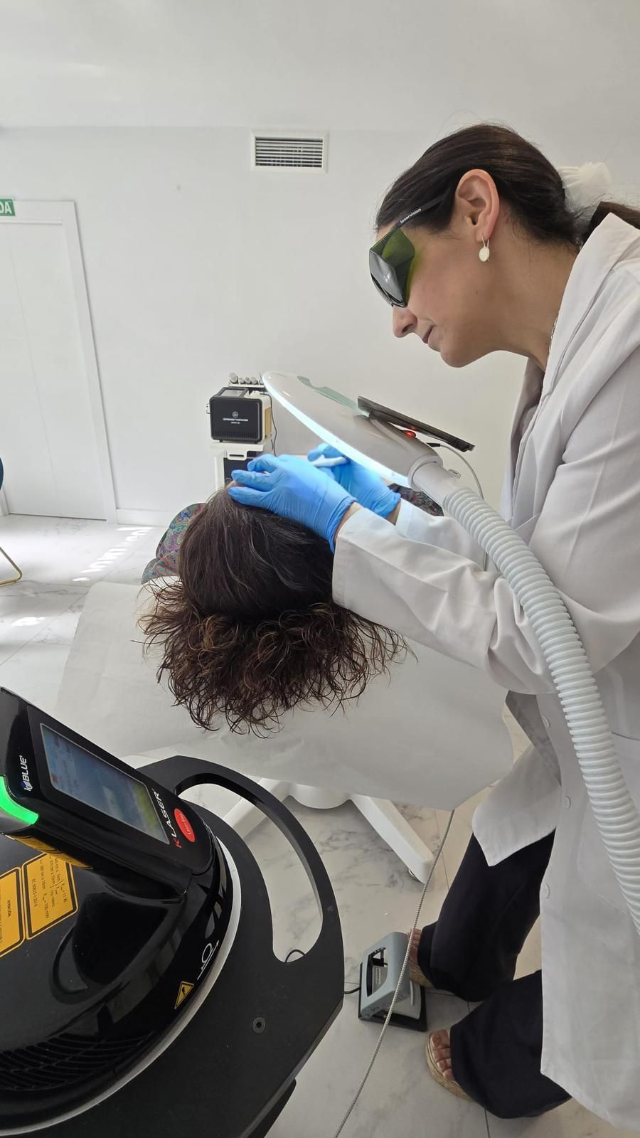 Rostro de mujer con marcas quirúrgicas, tocado con manos enguantadas y ojos cerrados.