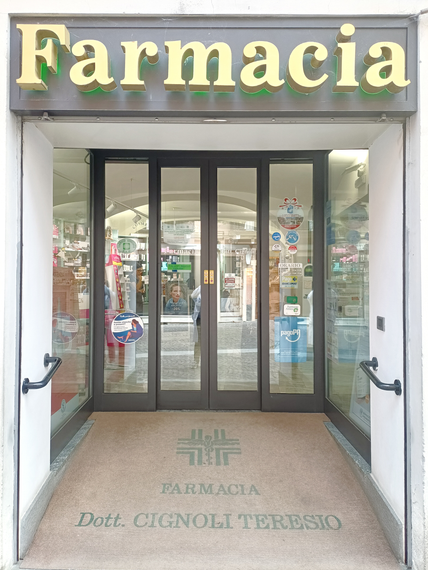 Una farmacista bionda in camice bianco prende i farmaci da uno scaffale in una farmacia ben illuminata.