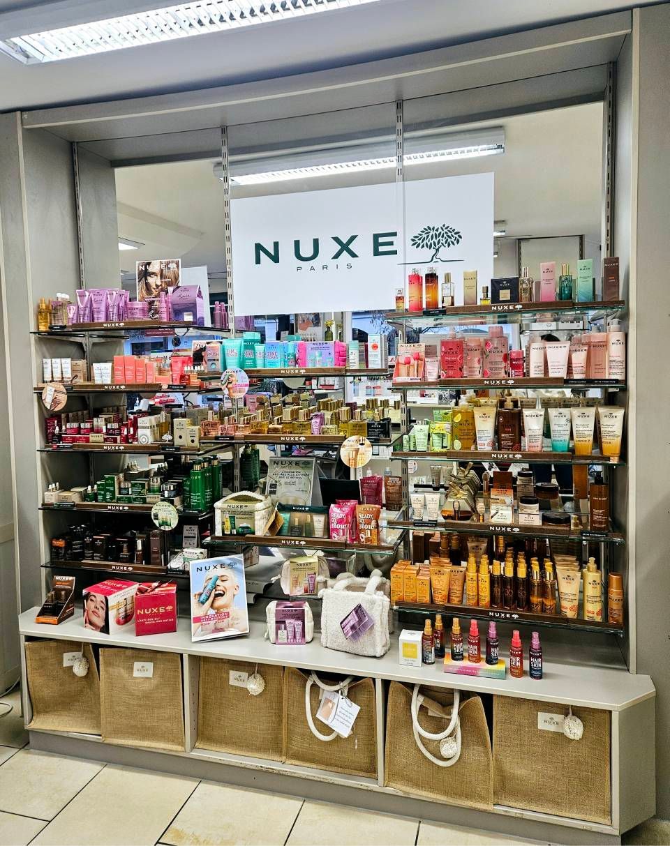 Présentoir de cosmétiques NUXE Paris dans un magasin, mettant en valeur divers produits colorés sur des étagères et dans des paniers tressés.