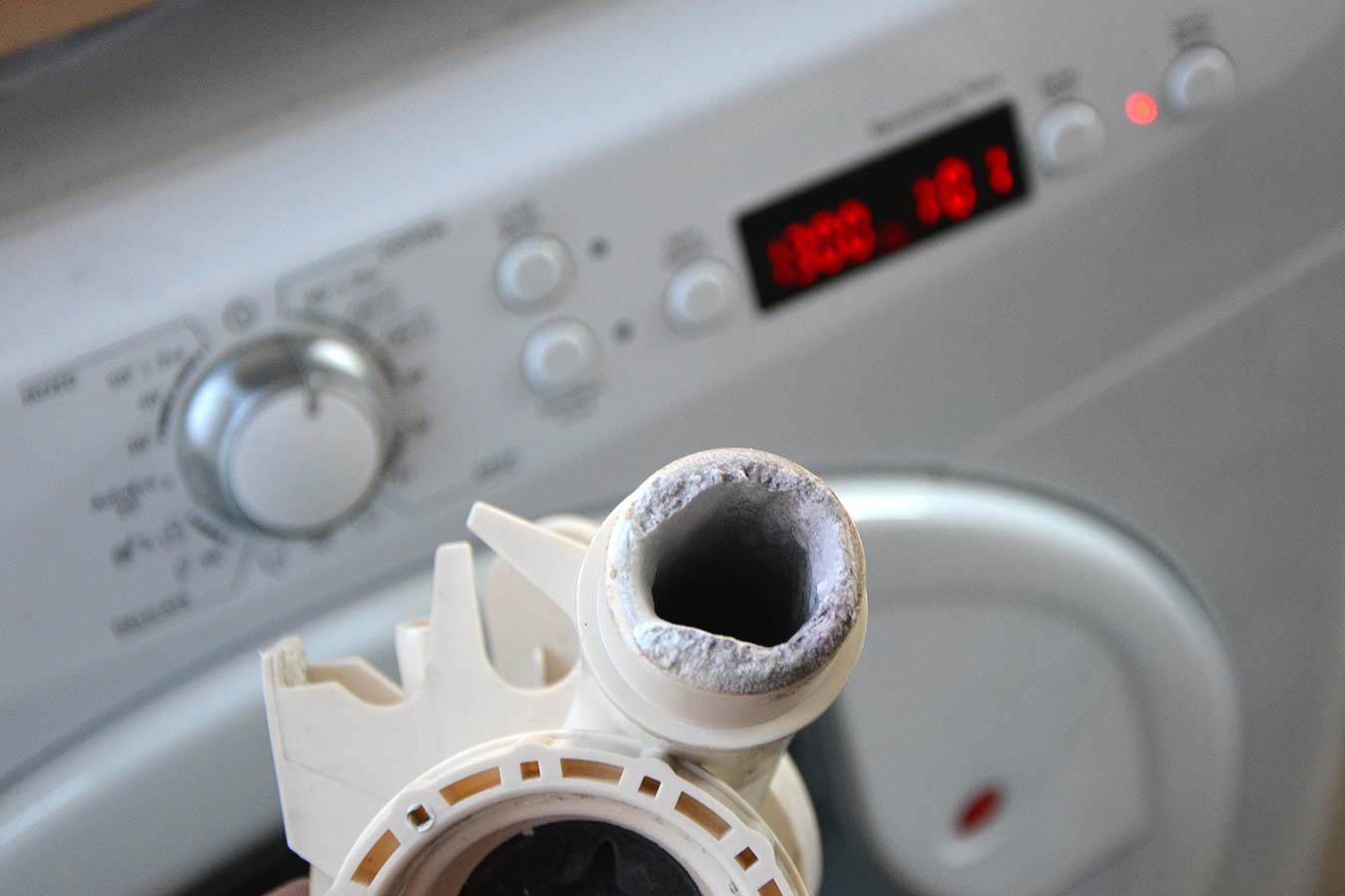 Un tuyau plein de tartre devant une machine à laver