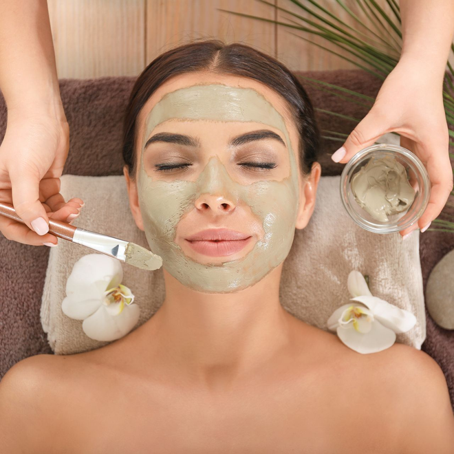 Personne en train d'appliquer un masque vert avec un pinceau sur le visage d'une femme
